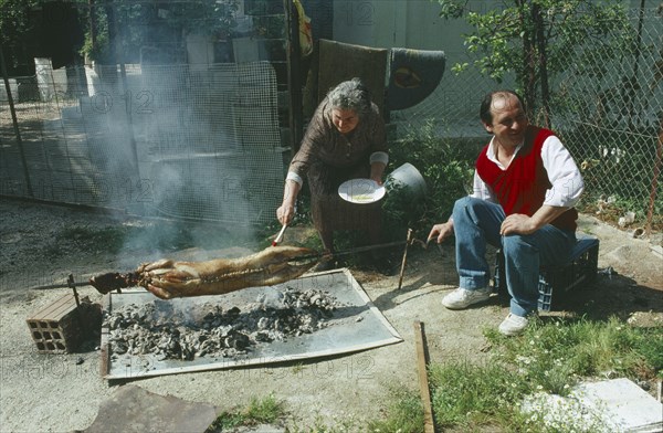 GREECE, Attica, Nea Makri, A couple roasting a lamb traditionally over coals outside at Easter.