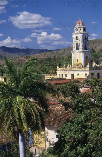 CUBA, Trinidad, Iglesia San Franciso de Paula roof and bell tower with red tiled rooftops and palm tree in the foreground.