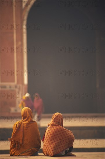 INDIA, Uttar Pradesh, Agra, Two woman sat talking in front of one of the red sand stone buildings that frame the Taj Mahal.