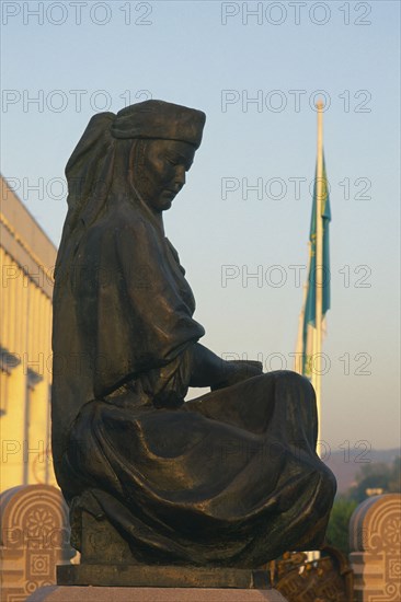 KAZAKHSTAN, Almaty, Stutue of person sat down and a flag pole behind.