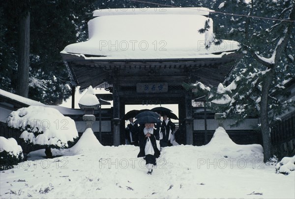 JAPAN, Honshu, Kii Peninsula, Mount Koya-san.  Venerated Shingon-Buddhist site.  Novice monks walking through gateway of temple complex in heavy snow.