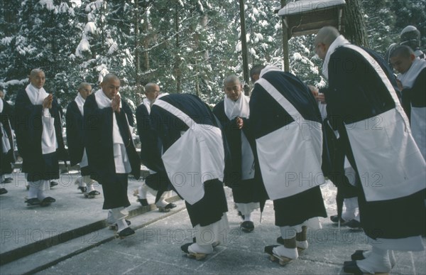 JAPAN, Honshu, Kii Peninsula, Mount Koya-san.  Venerated Shingon-Buddhist site.  Group of monks bow to each other in greeting.  Snow covered trees behind.