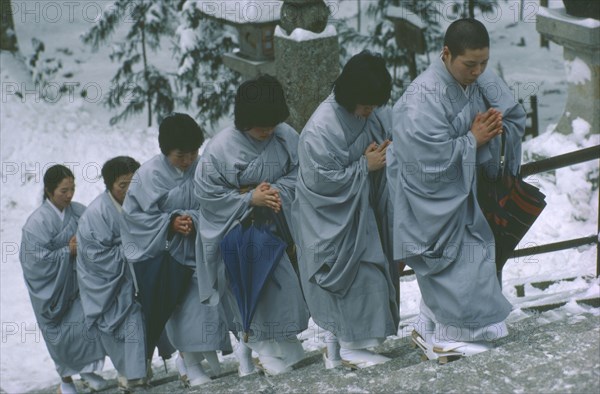 JAPAN, Honshu, Kii Peninsula, Mount Koya-san.  Venerated Shingon-Buddhist site.  Novice nuns climbing steps in heavy snow.