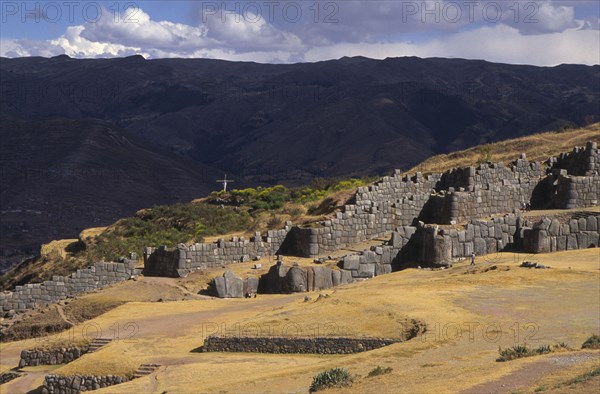 PERU, Cuzco, "Sacsayhuaman inca site, people walking round the old walls and a cross in the background."