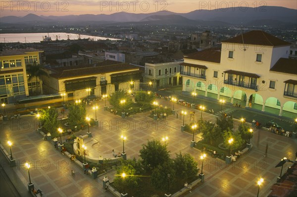 CUBA, Santiago de Cuba, Parque Cespedes at night.  Elevated view over paved square and surrounding buildings with people and street lights.