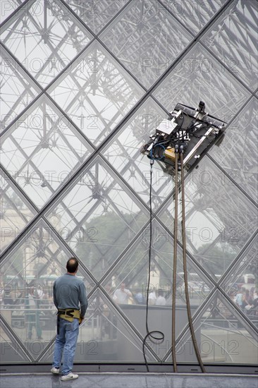 FRANCE, Ile de France, Paris, Workman watching robot window cleaning machine on the pyramid at the Louvre Museum