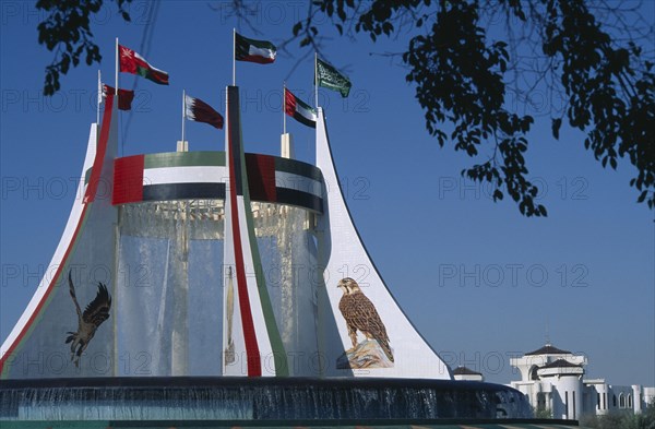 UAE, Abu Dhabi, Falcon Fountain with flags flying on the top framed by  tree branches. Part of the Hotel Intercontinental.
