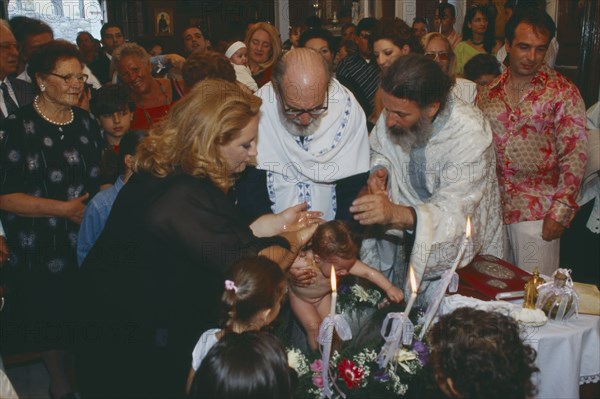 GREECE, Cyclades Islands, Syros, "A Greek orthodox christening, the child being held and water poured over him with friends and family watching from behind."
