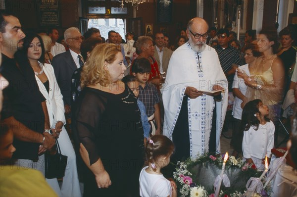 GREECE, Cyclades Islands, Syros, "A Greek orthodox christening, The Priest reads with friends and family watching from behind."