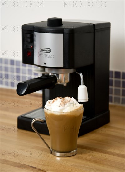 FOOD & DRINK, Coffee, Domestic Coffee machine on wooden kitchen worktop with a cup of cappuccino in a glass mug