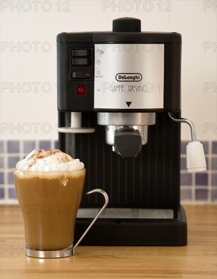 FOOD AND DRINK, Coffee, Domestic Coffee machine on wooden kitchen worktop with a cup of cappuccino in a glass mug