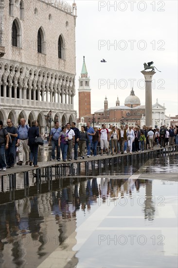 ITALY, Veneto, Venice, Aqua Alta High Water flooding in St Marks Square with tourists walking on elevated walkways outside the Doges Palace