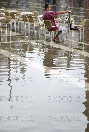 ITALY, Veneto, Venice, Aqua Alta High Water flooding in St Marks Square with an artist painting a watercolour seated at a table in the water of the flooded piazza Paul Seheult