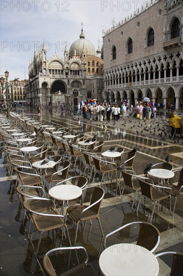 ITALY, Veneto, Venice, Aqua Alta High Water flooding in St Marks Square with restaurant tables in water by the Doges Palace with St Marks Basilica beyond
