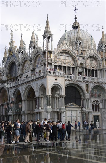 ITALY, Veneto, Venice, Aqua Alta High Water flooding in St Marks Square with tourists walking on elevated walkways above the water beside St Marks Basilic