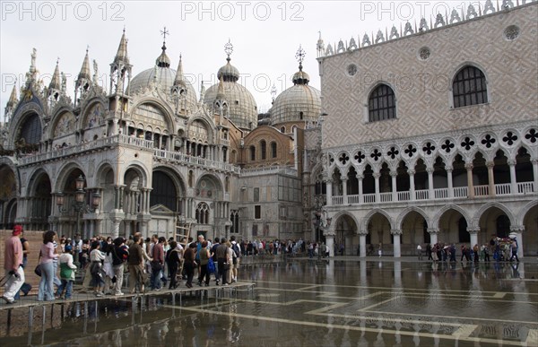 ITALY, Veneto, Venice, Aqua Alta High Water flooding in St Marks Square with tourists walking on elevated walkways above the water beside St Marks Basilica and the Doges Palac