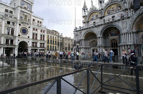 ITALY, Veneto, Venice, Aqua Alta High Water flooding in St Marks Square with tourists on elevated walkways above the flooded piazza beside St Marks Basilica and the Torre dell'Orologio clock tower