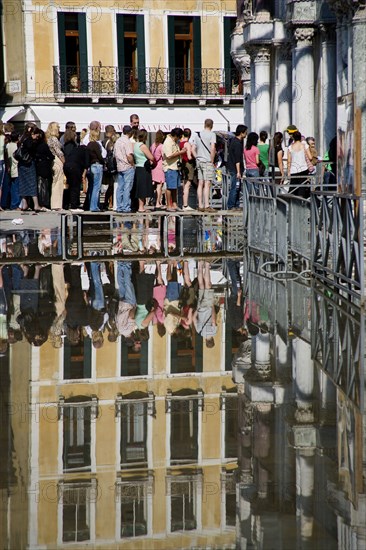 ITALY, Veneto, Venice, Aqua Alta High Water flooding in St Marks Square with tourists queuing on elevated walkways to enter St Marks Basilica