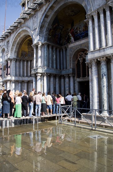 ITALY, Veneto, Venice, Aqua Alta High Water flooding in St Marks Square with tourists queuing on elevated walkways to enter St Marks Basilic