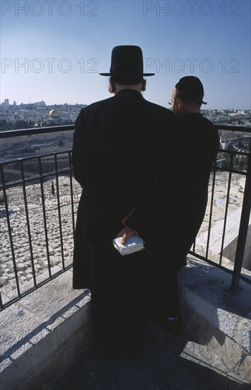 ISRAEL, Jerusalem, Two elderly Ultra Orthodox Jewish men one holding a bible in his hand surveying the cemetery on the Mount of Olives with the Old City in the background