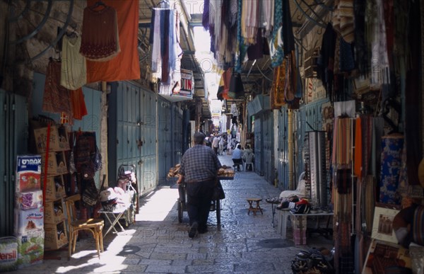 ISRAEL, Jerusalem, An Arab man pushing his bread cart through a narrow street between clothes and textile stalls in the Old City