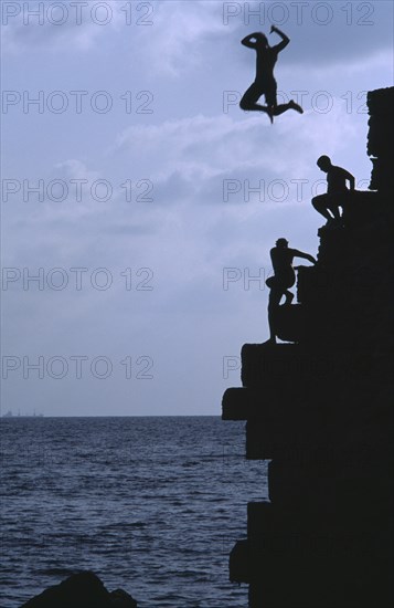 ISRAEL, Acre, Arab boys climbing the old harbour walls to jump into the sea with a boy leaping into the air at the top