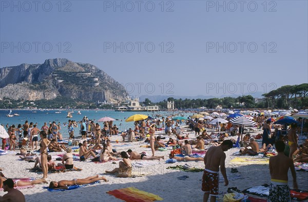 ITALY, Sicily, Palermo, Mondello Beach. View across busy sandy beach with sunbathers on sand towards the sea and hills seen from across water