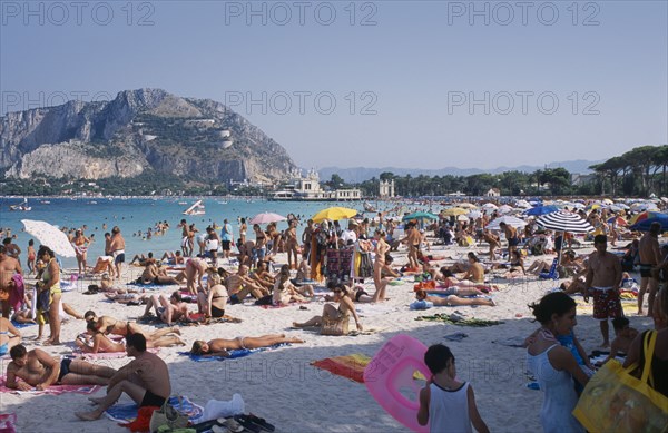 ITALY, Sicily, Palermo, Mondello Beach. View across busy sandy beach with sunbathers on sand towards the sea and hills seen from across water
