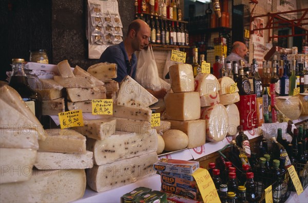 ITALY, Sicily, Catania, Market cheese stall with a male stall holder displaying a selection of cheeses and olive oil with euro money price signs