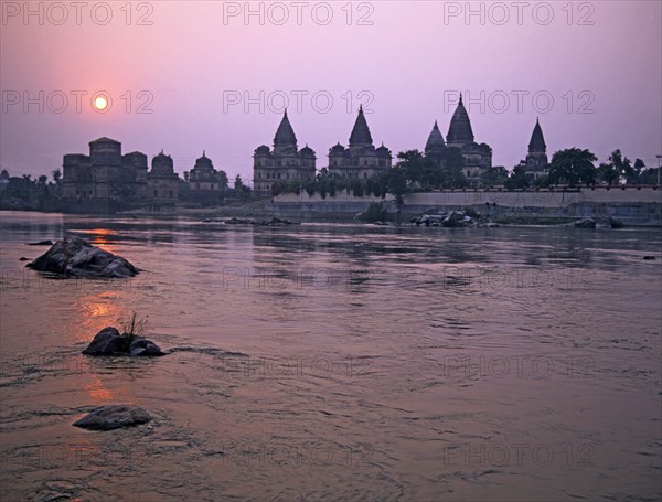 INDIA , Madhya Pradesh, Orchha, The domes and spires of the chhatris memorials to Bundelkhand's former rulers from across the Betwa River at sunset