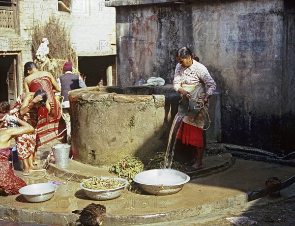 NEPAL, Khokana, One of the villagers drawing water and others washing their hair at the village well in this Newari farming village in the Kathmandu Valley.