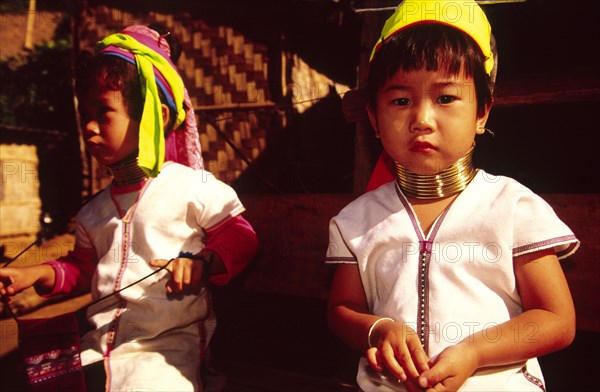 THAILAND, North, Mae Hong Son, "Nai Soi Long neck Karen children. Originally from Myanmar, the Long neck Karen (Padaung) people fled persecution in their native land and settled across the border in Thailand where they have become something of a tourist attraction. This new life has provided them with both a steady income and a stable environment. From an early age, Padaung girls wear the traditional bronze rings on their necks and legs. As the rings are added over the passing years, their necks elongate. Once fastened the rings remain throughout their lives."