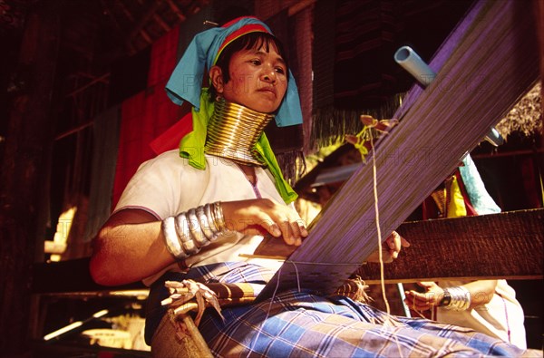 THAILAND, North, Mae Hong Son, "Nai Soi Long neck Karen woman weaving. Nai Soi near the Thai border with Myanmar, is one of several villages where refugee Karen tribals have set up home and use tourism to sustain them. Their necks and legs are traditionally hidden behind an increasing succession of bronze rings which the women must wear from an early age"