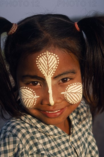 MYANMAR, Amarapura, Head and shoulders portrait of young girl at U Bein Bridge near Mandalay wearing thanakha paste patterns on her face to beautify and protect skin from the sun.