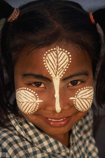 MYANMAR, Amarapura, Head and shoulders portrait of young girl at U Bein Bridge near Mandalay wearing thanakha paste patterns on her face to beautify and protect skin from the sun.