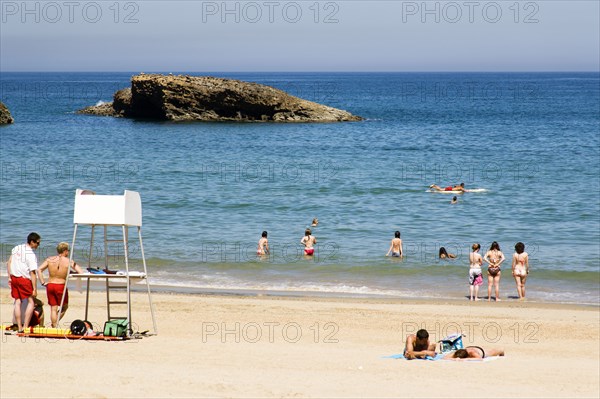 FRANCE, Aquitaine Pyrenees Atlantique, Biarritz, The Basque seaside resort on the Atlantic coast. Lifeguards and young tourists on the Grande Plage beach with a man paddling on a surfboard off the beach