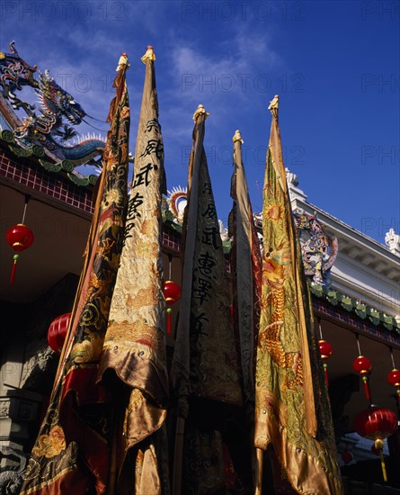 MALAYSIA, Penang, Georgetown, Chinese temple roof hung with red lanterns for Chinese New Year with richly embroidered flags in the foreground.