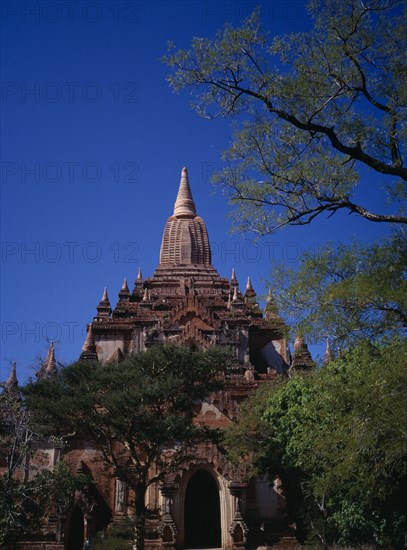 MYANMAR, Bagan, Shwegugyi Pahto or Great Golden Cave in old city.  Exterior framed by trees showing decorated style with tall ‘corncob’ sikhara above sanctum stressing vertical line.