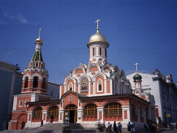 RUSSIA, Moscow, "Exterior of refurbished church with red and white painted facade, gold domed roof and painted icons above the entrance."