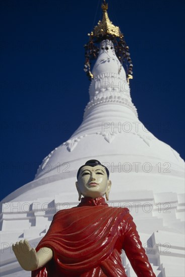 MYANMAR, Religion, Buddhism, White stupa at newly painted temple on road to Mandalay with standing Buddha in pose with extended right arm with open palm turned to front.