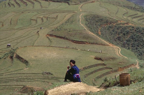 VIETNAM, North, Sapa, Hmong woman sitting on hillside overlooking agricultural terraces.