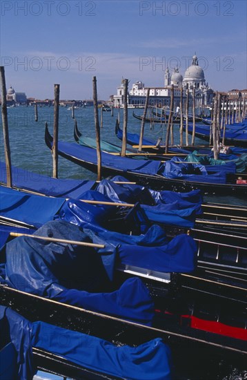 ITALY, Veneto, Venice, Line of gondolas moored at Piazza San Marco jetty with Santa Maria della Salute in distance behind.