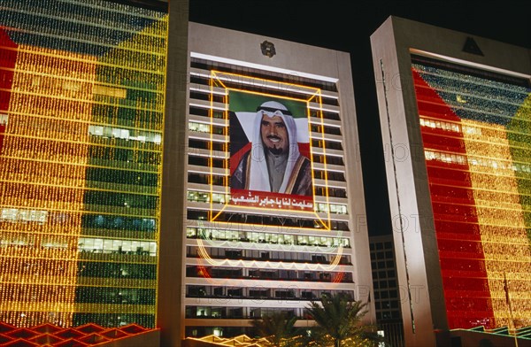KUWAIT, Illuminated Buildings, Portrait of the former Amir HH Sheikh Sabah Al-Ahmad Al-Jaber Al-Sabah flanked by Kuwait flag made from strings of illuminated lights on building at night.