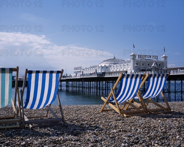 ENGLAND, East Sussex, Brighton, Blue and white striped deckchairs on pebble beach over looking Brighton Pier.