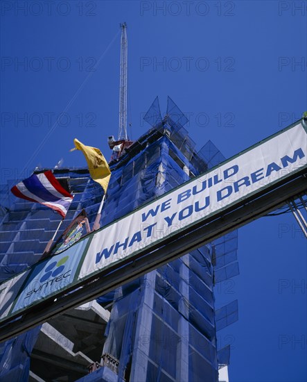 THAILAND, Bangkok, Looking up at sign ‘We Build What You Dream’ with high rise building under construction behind.