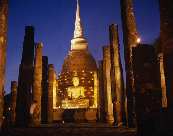 THAILAND, Sukhothai, Colonnade leading to massive seated Buddha and stupa illuminated at dusk during Loi Krathong festival of lights.