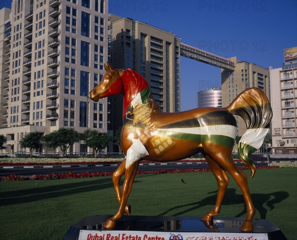 UAE, Dubai, Brightly painted statue of horse with advertising for Dubai Real Estate Centre set in formal grounds with hotel and high rise buildings behind.