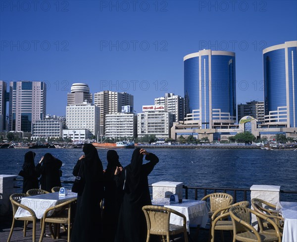 UAE, Dubai, Dubai Creek.  Women in waterfront restaurant on Bur Dubai city side looking out towards city skyline on Deira side.