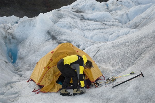 CHILE, "Southern Patagonia,", Glacier Chico, Mountaineer attaching crampons to his boots in front of tent set up in a crevasse.Trek from Glacier Chico (Chile) to El Chalten (Argentina)
