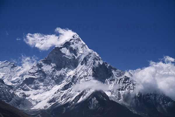 NEPAL, Himalayas, Khumbu Region, Mount Ama Dablam.  Snow covered peak of west face in drifting cloud against blue sky in May.